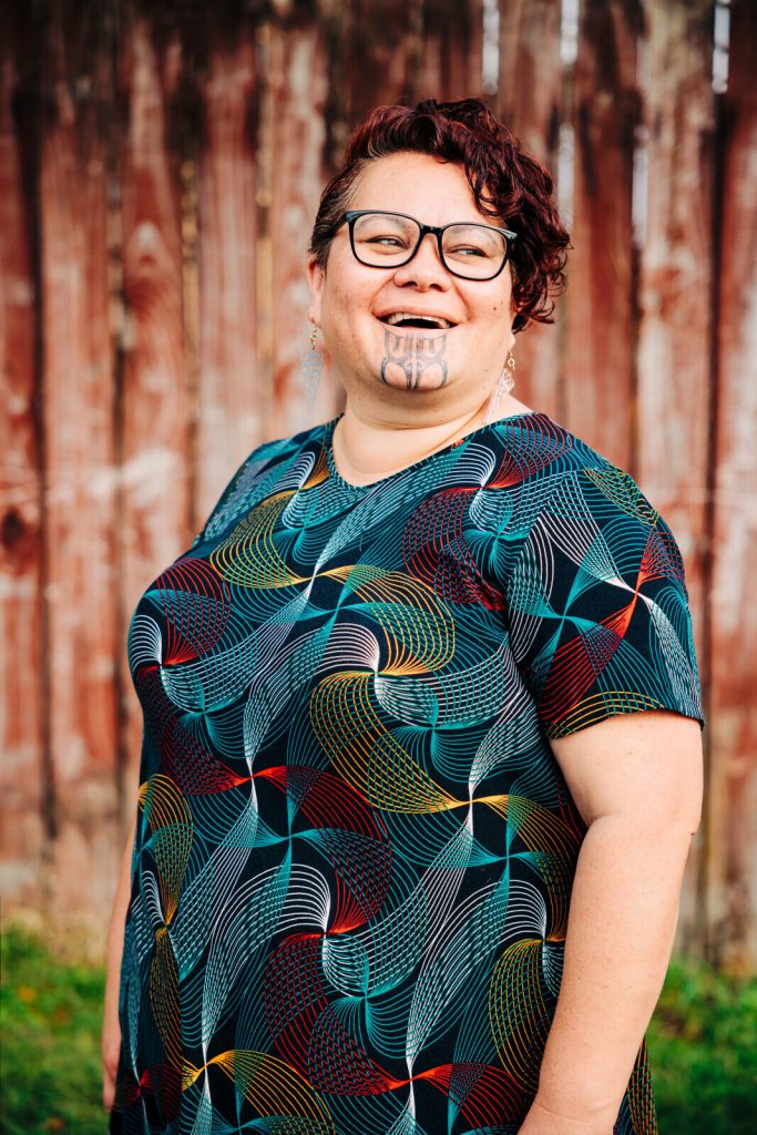 A smiling middle aged Māori woman with a moko kauae.
