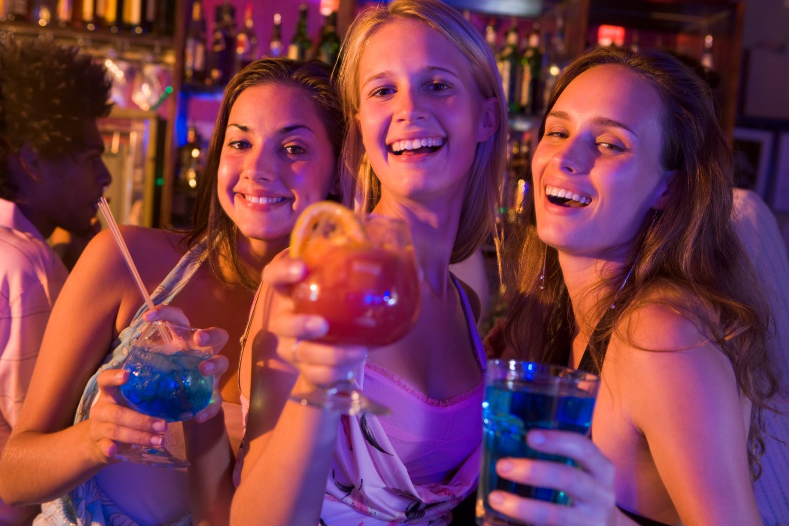 Three girls smiling and holding cocktails.