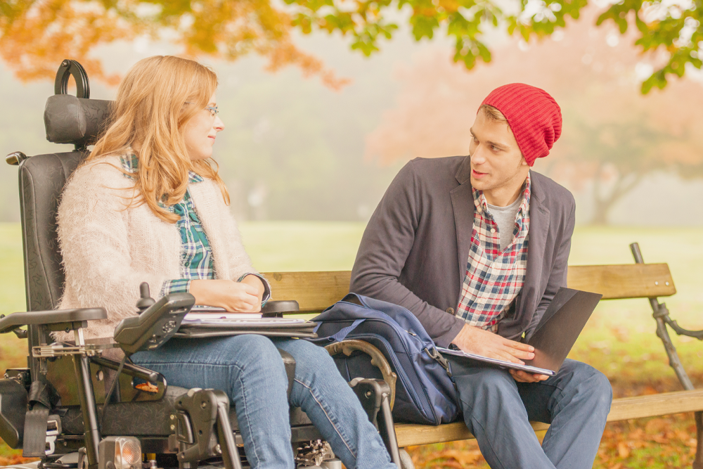A young man talks to a young woman in a wheelchair.